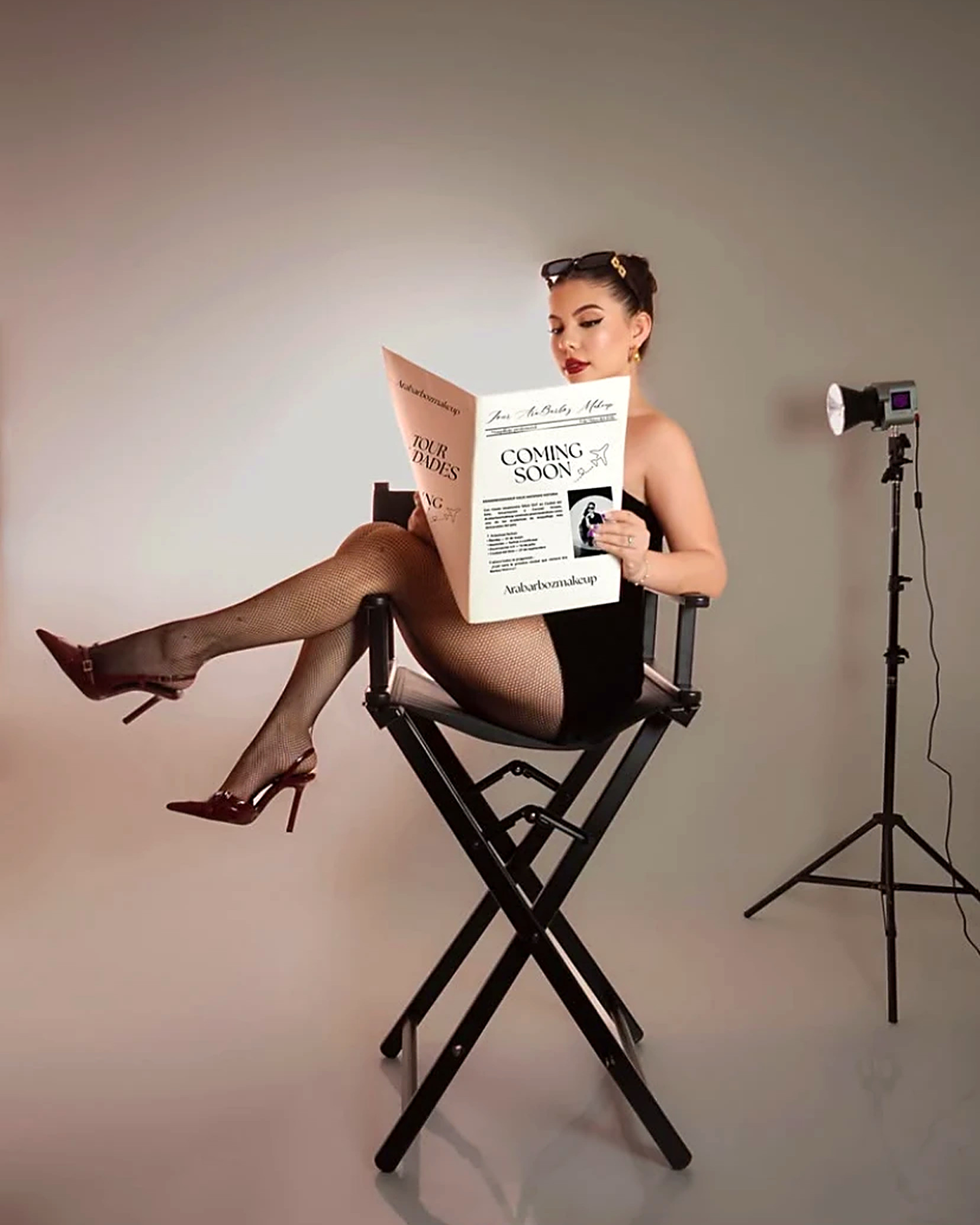 Ara Barboz sentada en una silla de maquilladora, leyendo un diario de la academia en un estudio de fotos