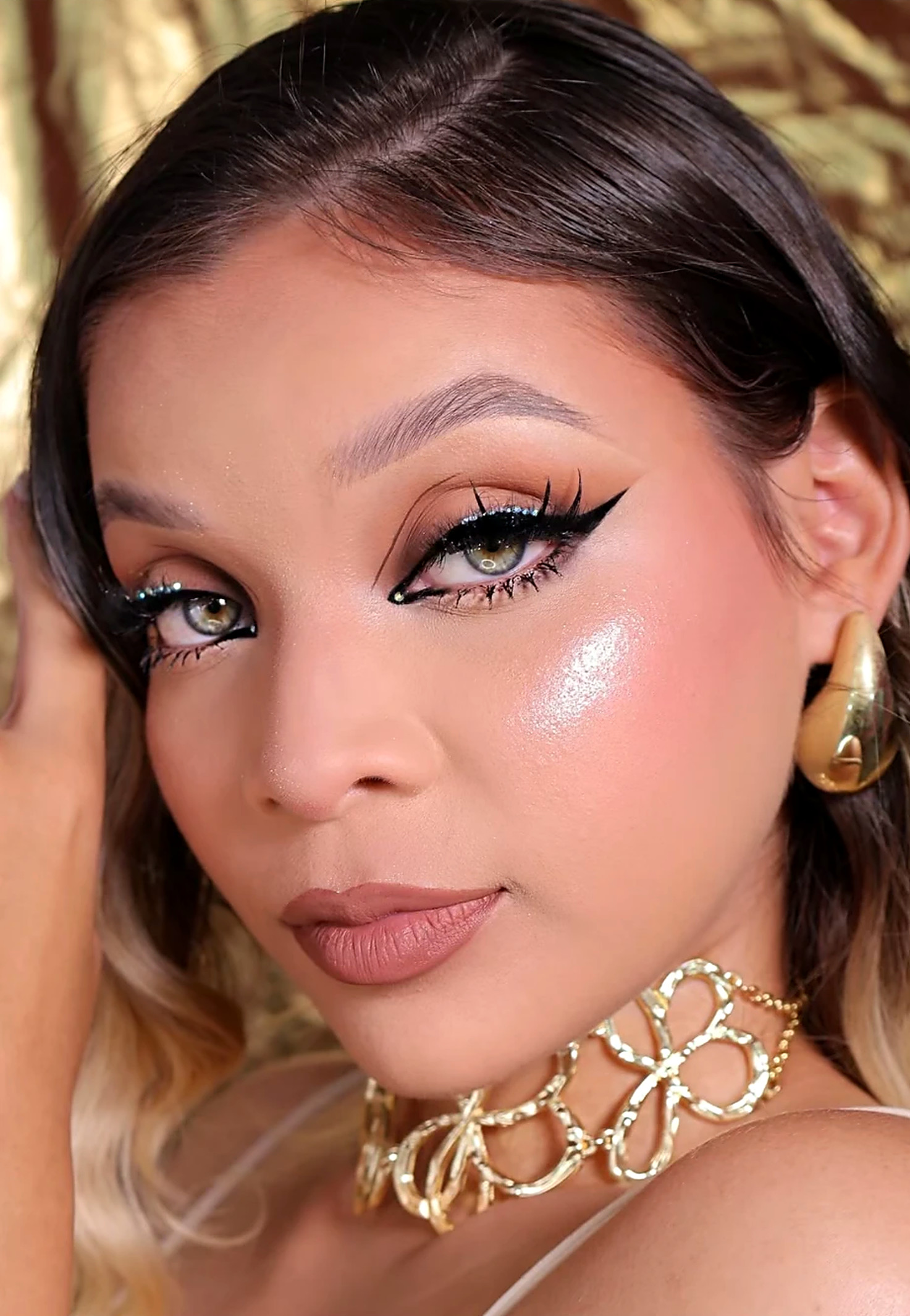 Maquillaje con delineado gráfico, brillo en el pómulo y labios nude, hecho por Ara Barboz